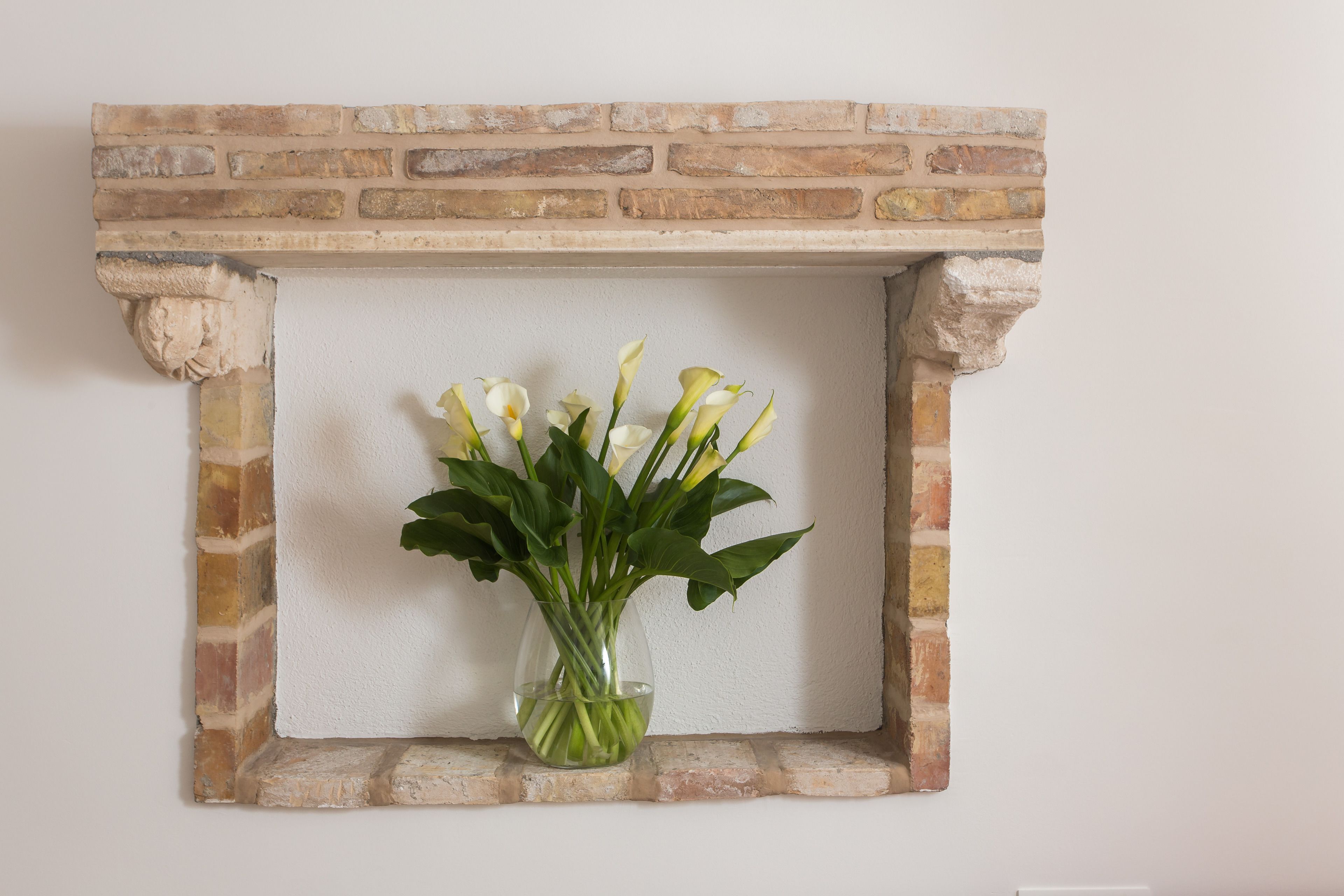 A framed picture with a vase of white flowers on a brick wall.