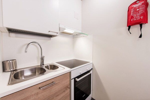 A compact kitchen with a stainless steel sink, a built-in oven, and a glass shelf above the stove. - Forenom Aparthotel Espoo Leppävaara (Espoo)