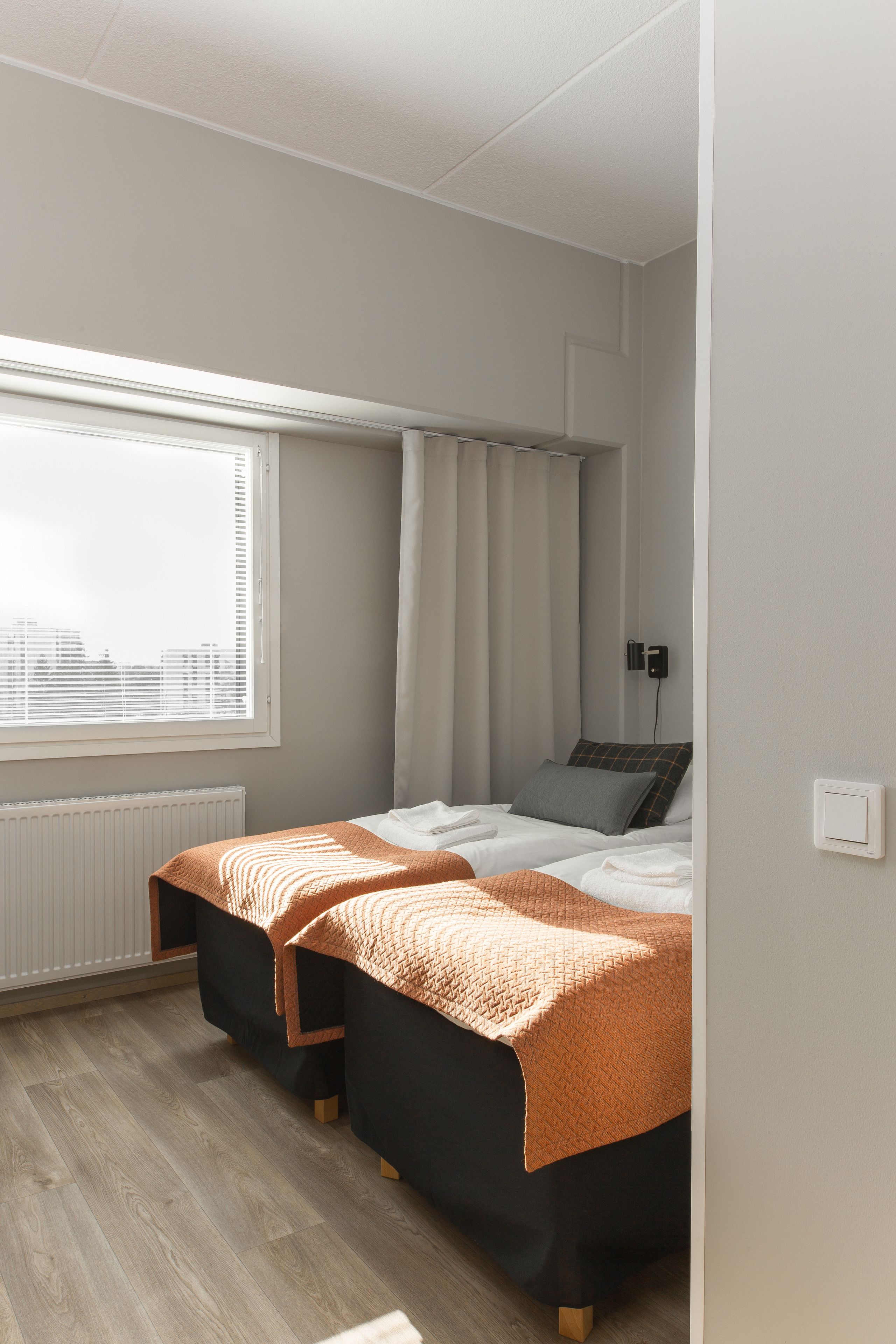 A bedroom with two beds, a window with blinds, a radiator, and a wall-mounted phone.