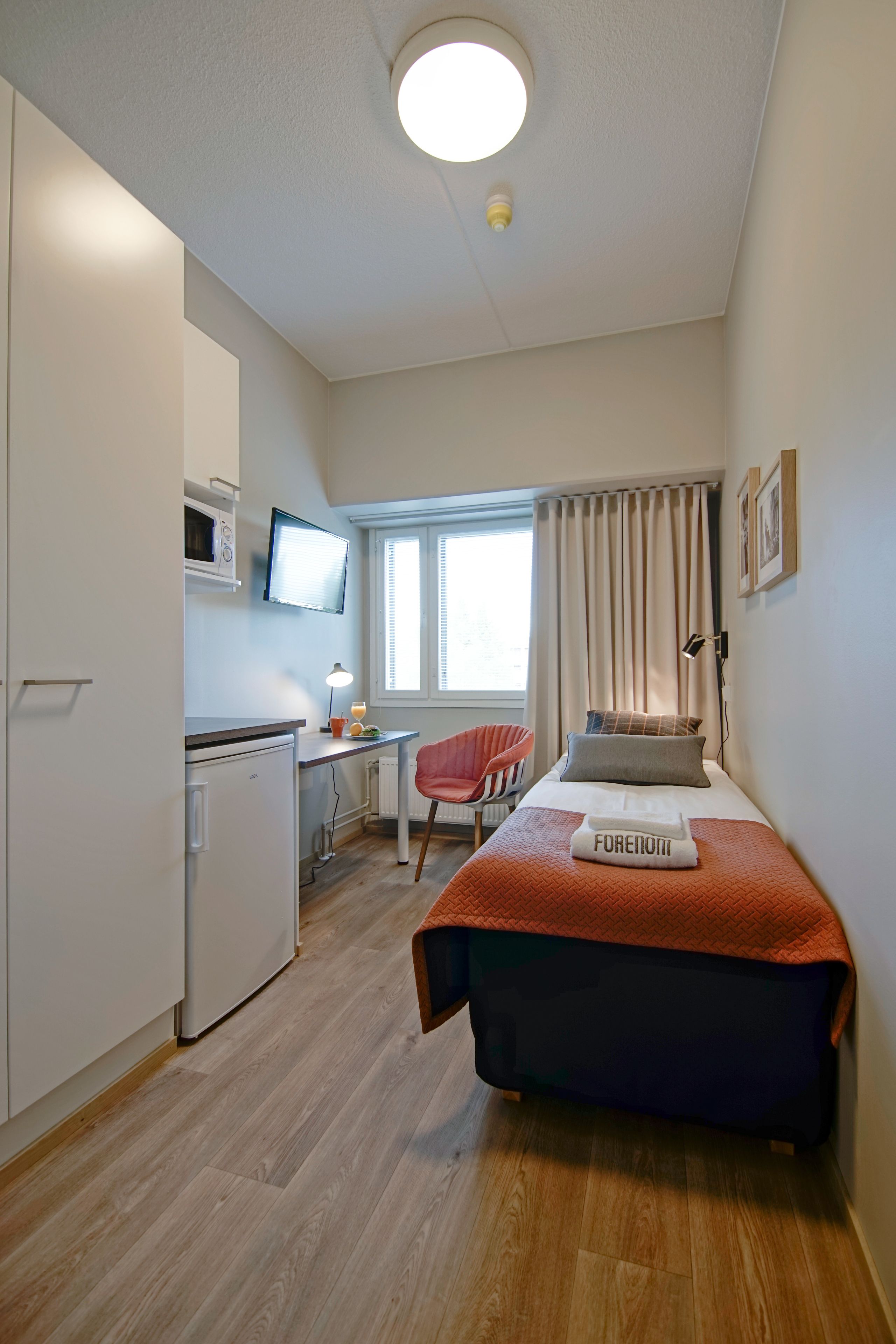 A compact room with a bed, a desk, a chair, a microwave, and a television.