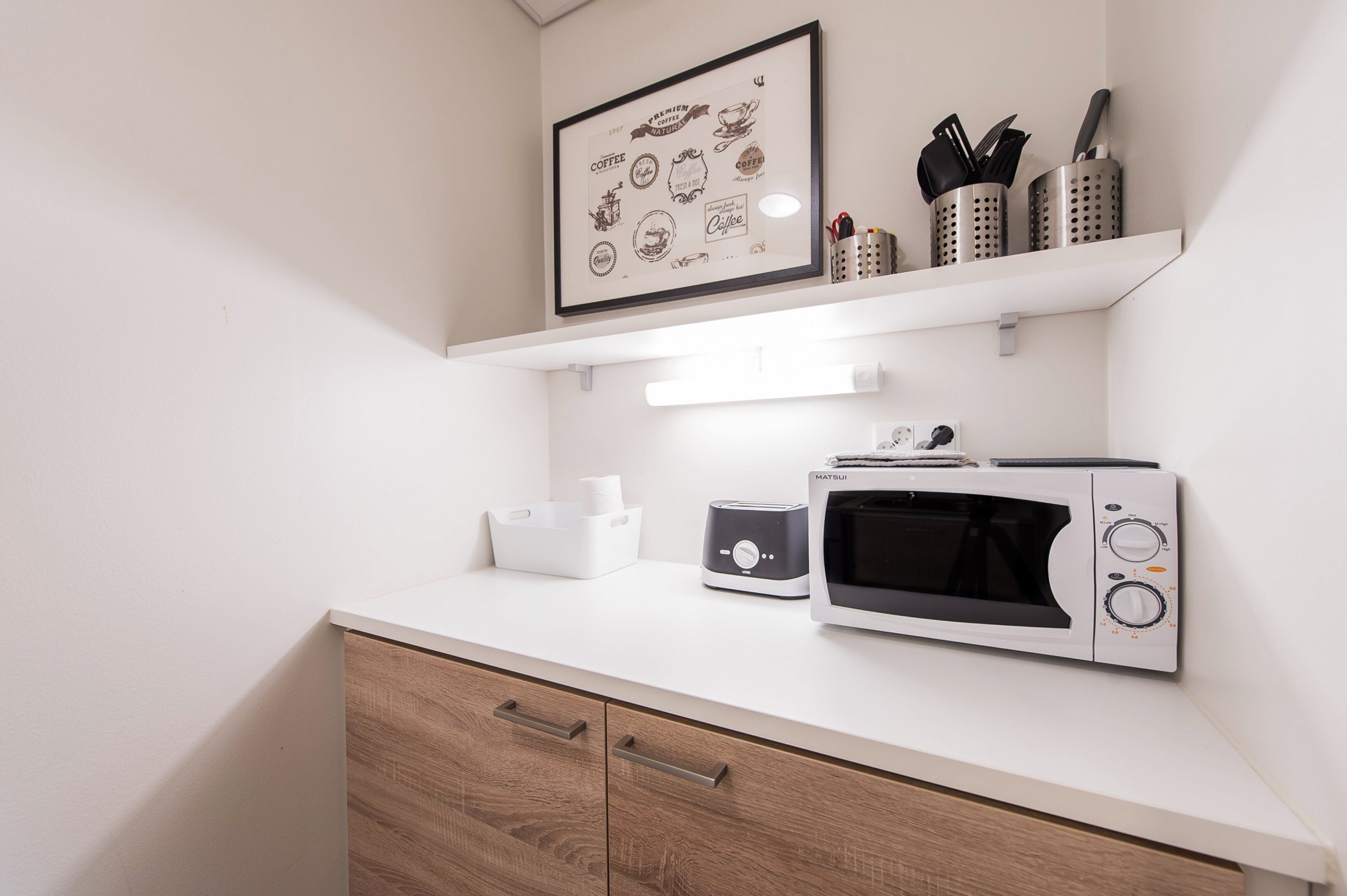 A kitchen with a microwave, toaster, and a framed coffee-themed artwork above the counter.