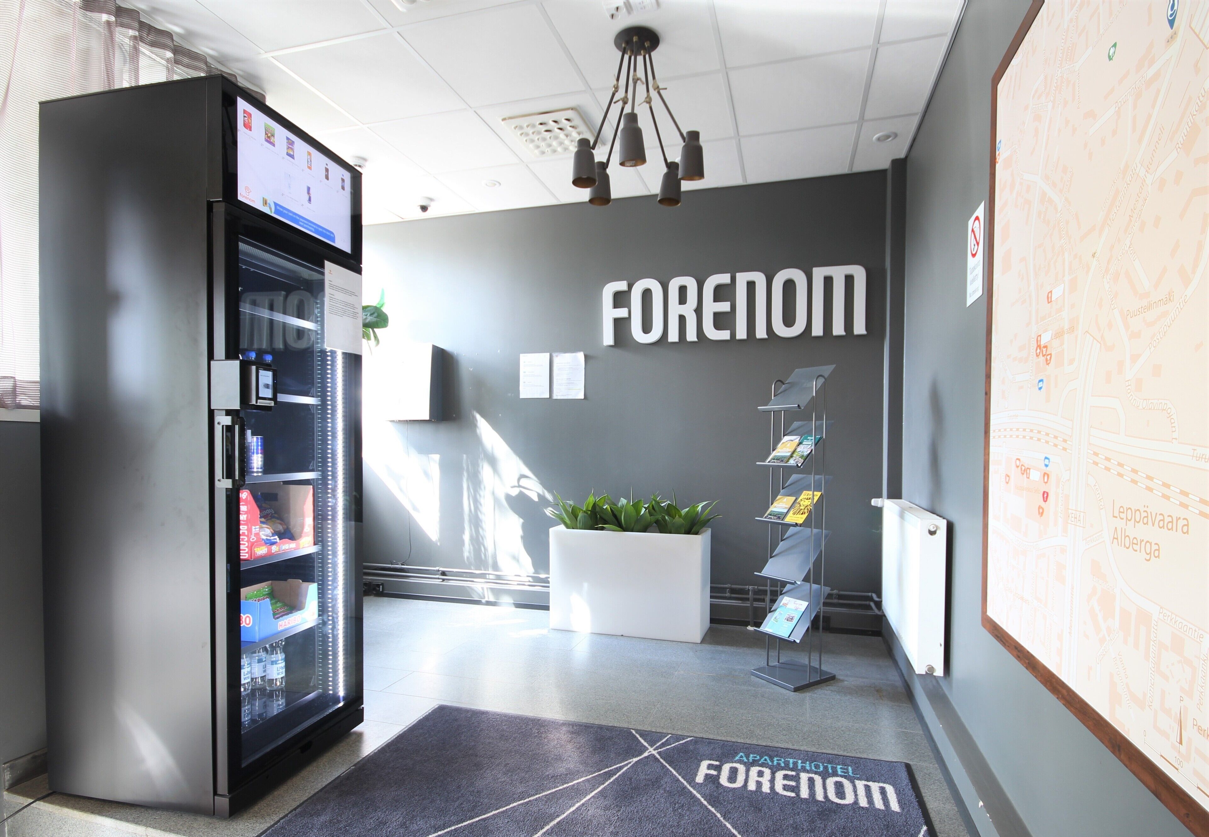A modern lobby with a vending machine, a potted plant, a map on the wall, and a sign that reads "FORENOM".