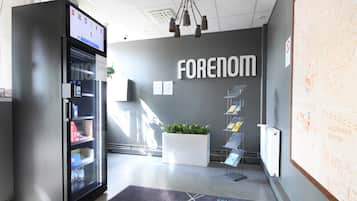 A modern lobby with a vending machine, a potted plant, a map on the wall, and a sign that reads "FORENOM".