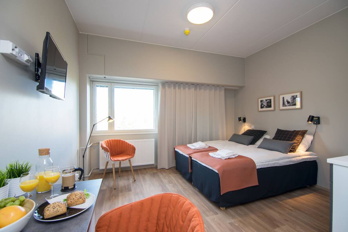 Ein modernes Hotelzimmer mit einem Bett, zwei Stühlen, einem Schreibtisch mit Frühstück und einem Fernseher.