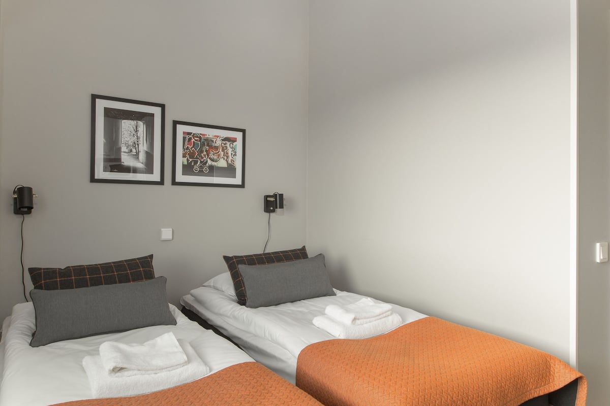 Ein Hotelzimmer mit zwei Betten, jeweils mit Kissen, Decke und Handtuch. An der Wand befinden sich zwei gerahmte Bilder.