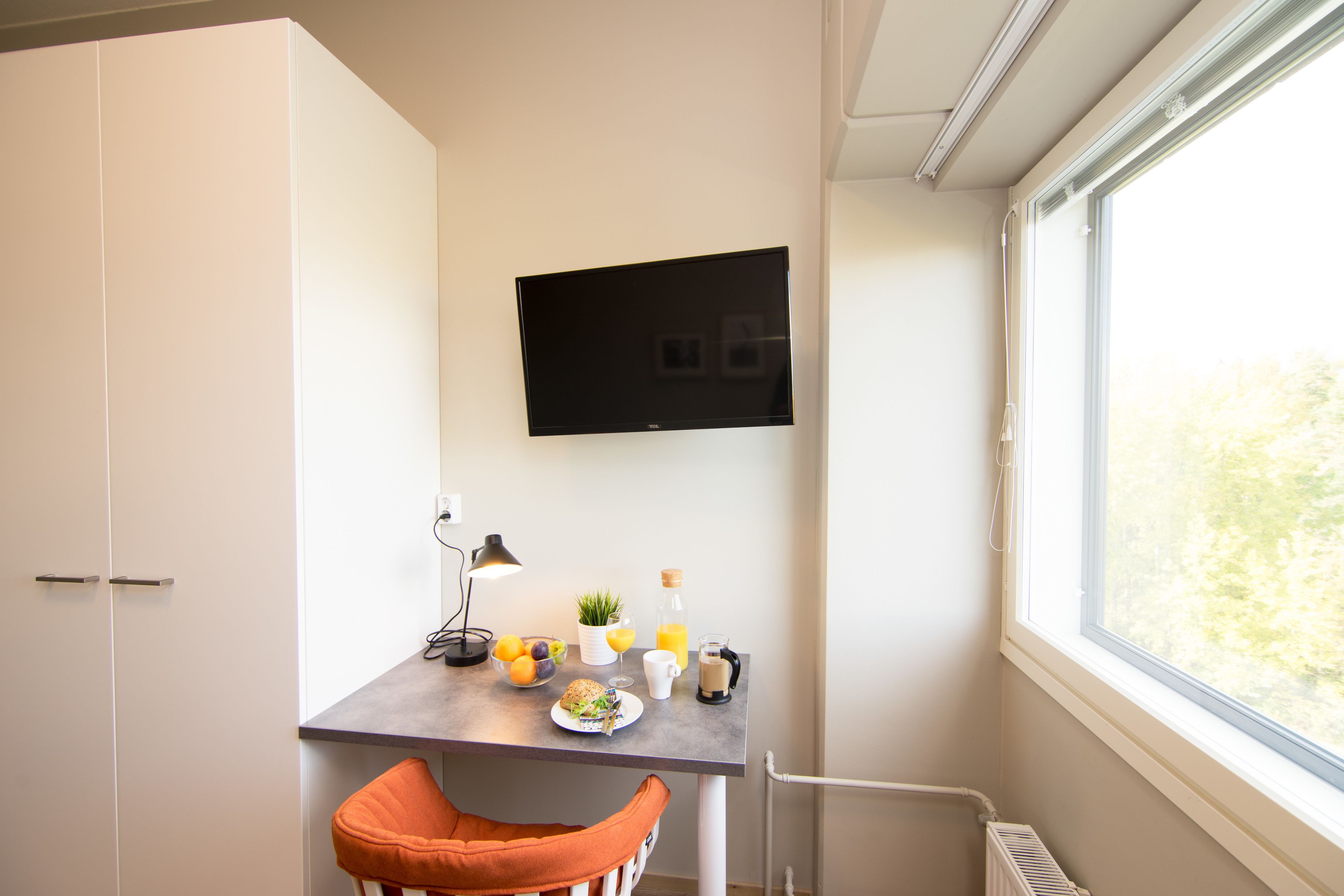 Une chambre moderne équipée d’un bureau, d’une chaise, d’un téléviseur et d’une fenêtre donnant sur la verdure.