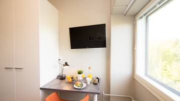 Une chambre moderne équipée d’un bureau, d’une chaise, d’un téléviseur et d’une fenêtre donnant sur la verdure.