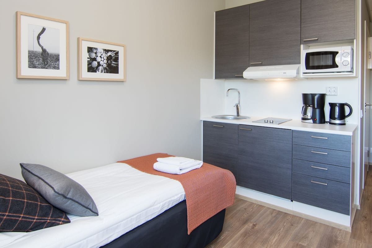 Ein gemütliches Schlafzimmer mit Bett, einer kleinen Küchenzeile mit Mikrowelle und Spüle. An der Wand befinden sich gerahmte Bilder.