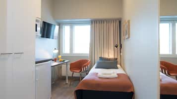 Kompakti hotellihuone, jossa on sänky, työpöytä tuolilla, televisio ja ikkuna, jossa on verhot.