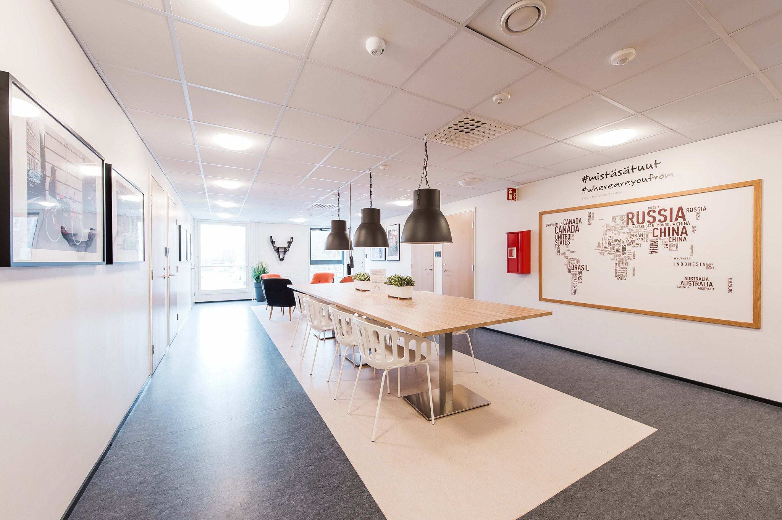 A modern office space with a long table, white chairs, pendant lights, and a wall with a map of Russia and other countries.
