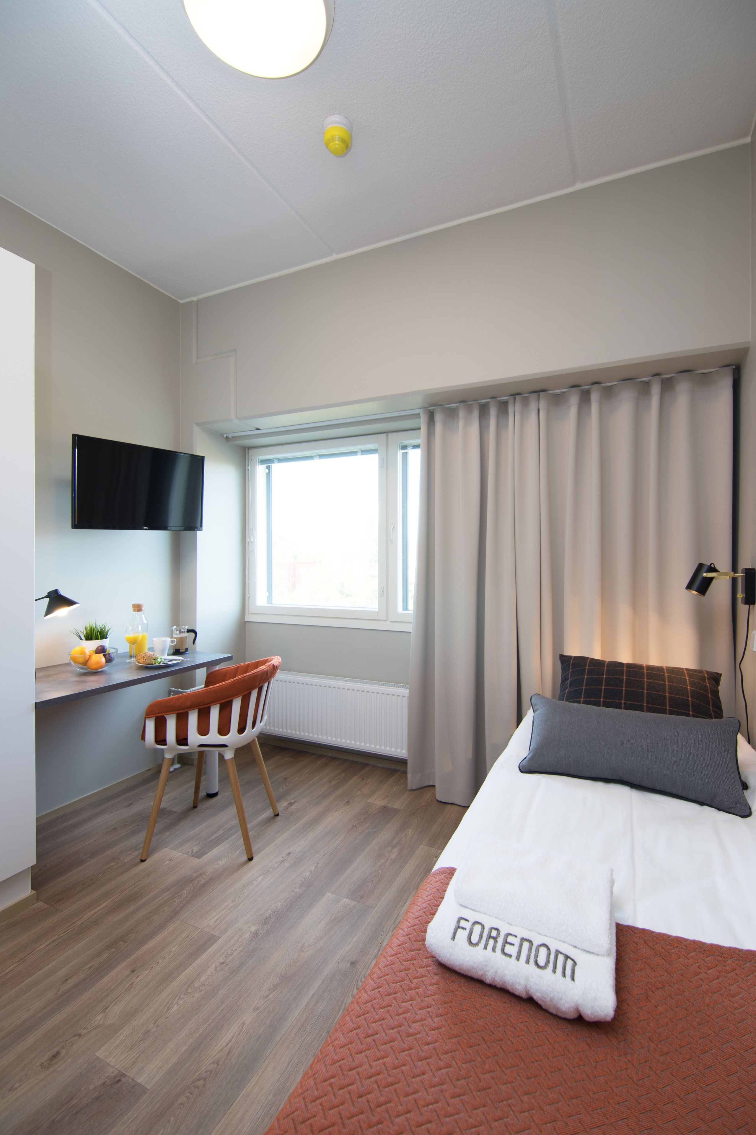 Una habitación de hotel moderna con una cama, un escritorio con una silla, un televisor y una ventana con cortinas.