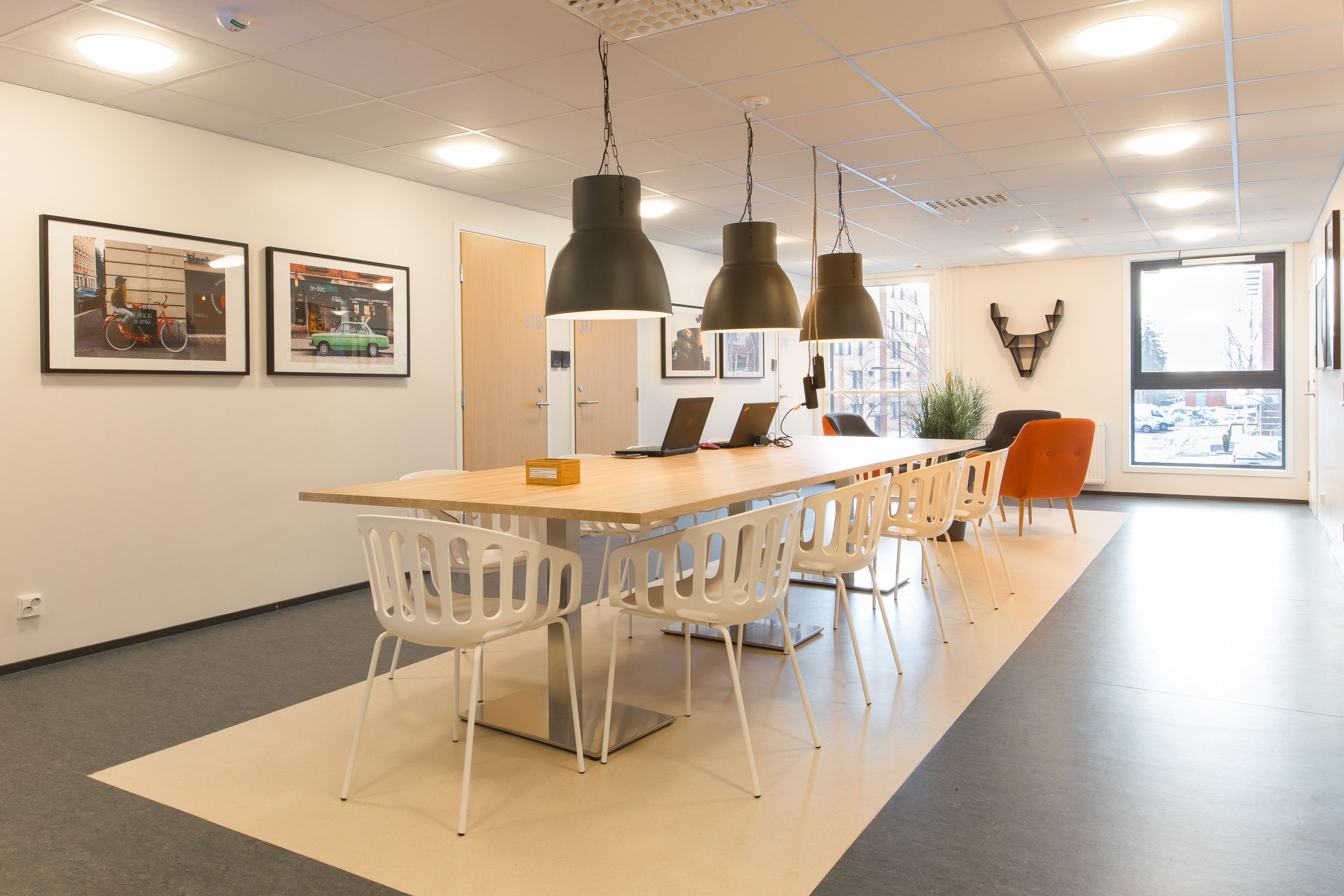 A modern office space with a long table, white chairs, and pendant lighting.