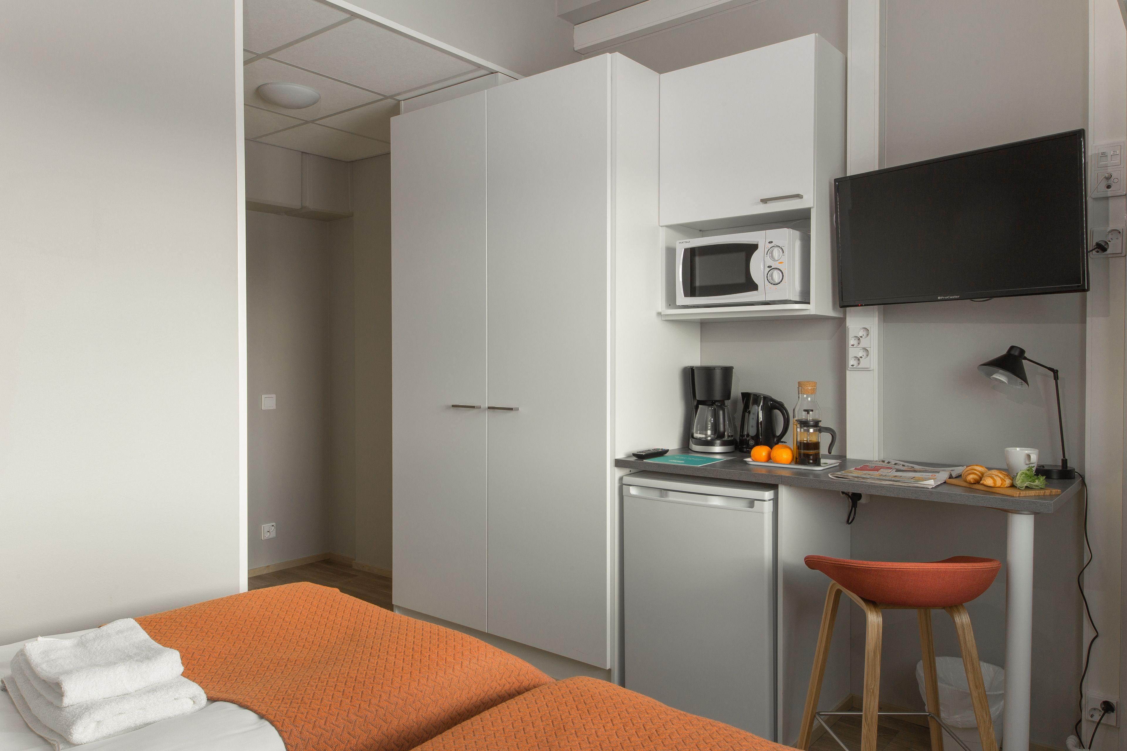 Una habitación de hotel compacta con una cama, kitchenette, microondas, cafetera y televisión.