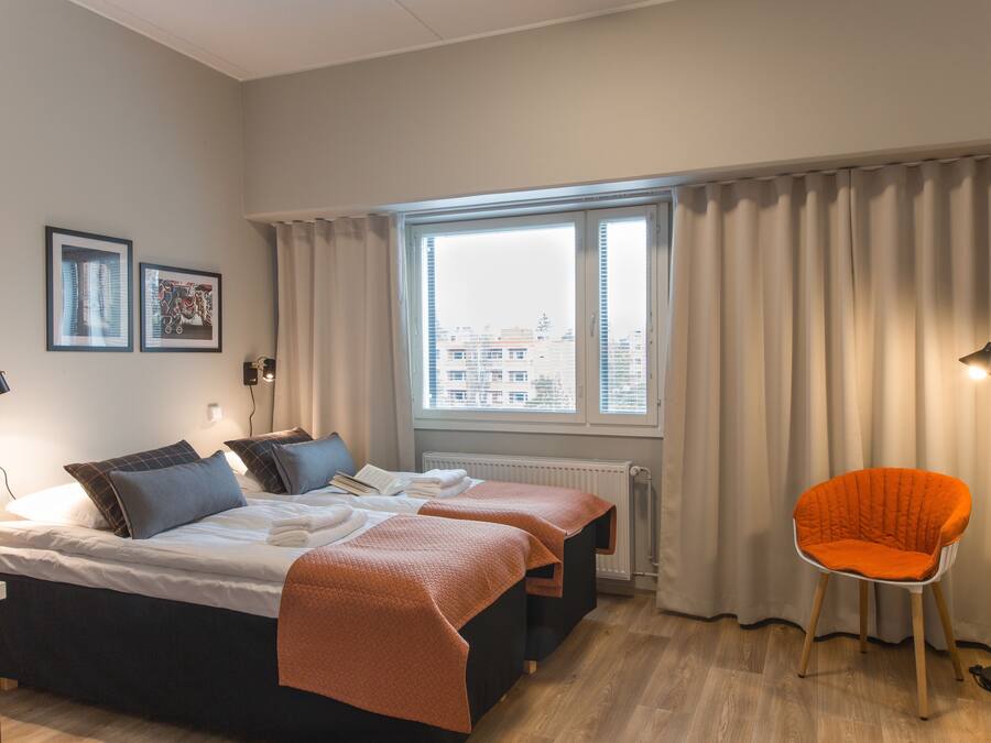 Een hotelkamer met een bed, twee nachtkastjes, een stoel, een raam met gordijnen en uitzicht op de stad.