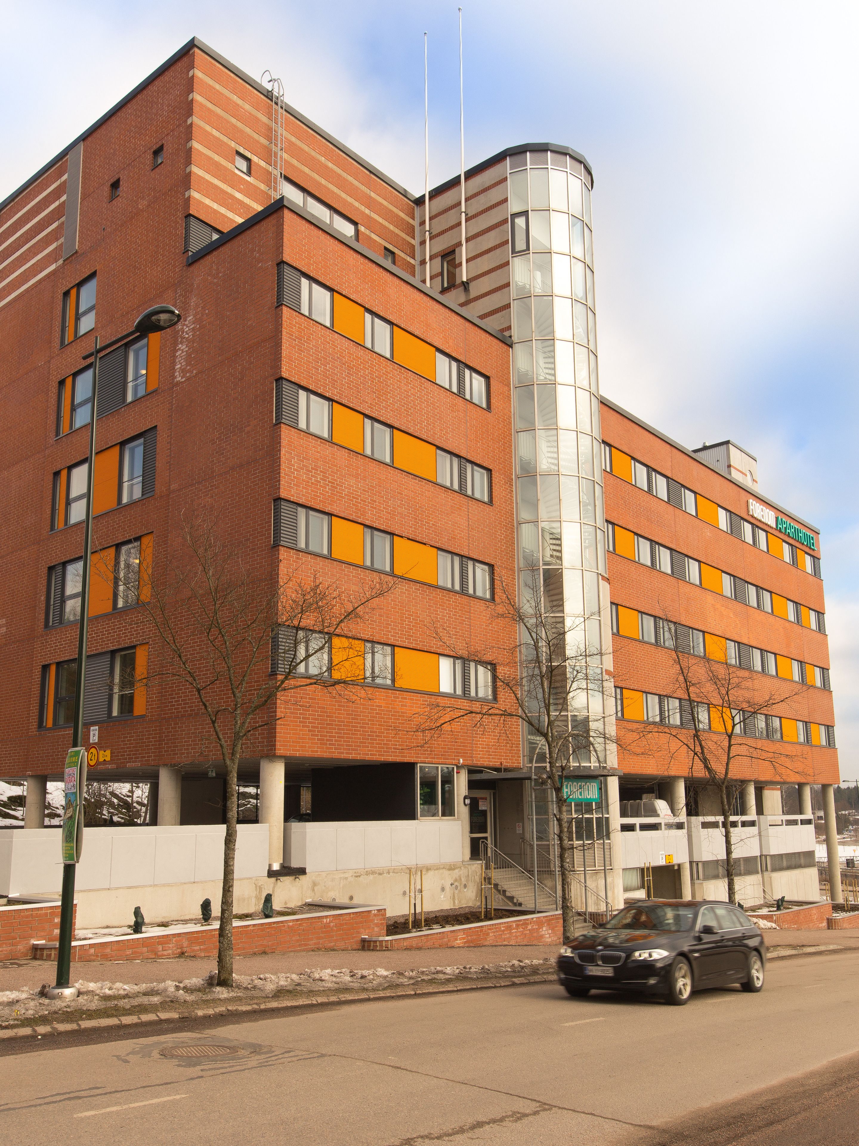 A multi-story building with a distinctive curved glass section, red brick facade, and orange window accents.