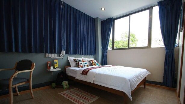 Un dormitorio con cama, una silla, una mesita de noche y un ventanal con cortinas.