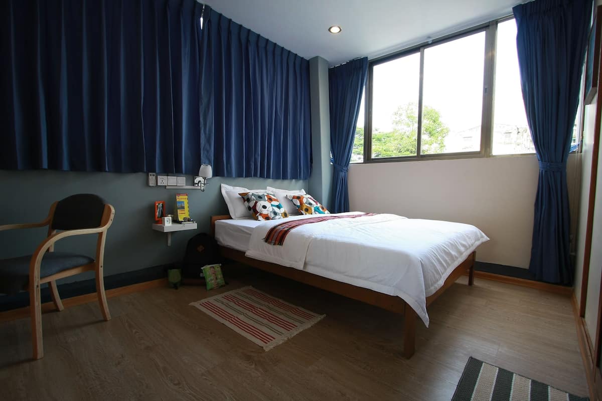 Ein Schlafzimmer mit einem Bett, einem Sessel, einem Nachttisch und einem Fenster mit Vorhängen.