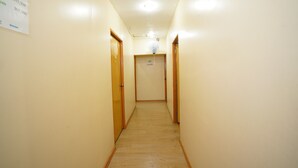 Un pasillo estrecho con puertas de madera a ambos lados, un cartel con los números de las habitaciones y un ventilador de techo.
