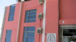 Un edificio rosa con varias unidades de aire acondicionado, un letrero que indica '15th Street @ Downtown Yangon' y un ventanal con cortina.