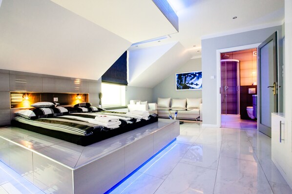 A modern bedroom with a large bed, a built-in desk, and a TV on the wall.