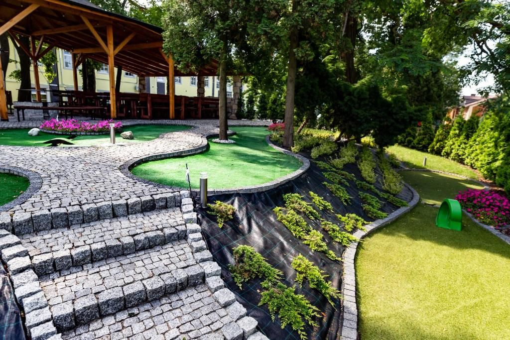 Un jardín ajardinado con zona pavimentada, un espacio de estar cubierto y una variedad de plantas.