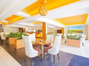Un moderno vestíbulo de hotel con zona de comedor central, arreglos de asientos y plantas decorativas.