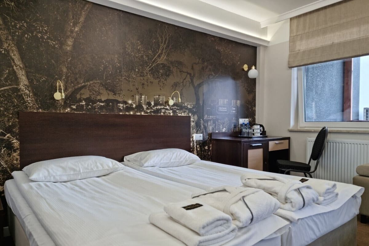 Une chambre d’hôtel avec deux lits, un bureau, une chaise et une fenêtre donnant sur le panorama de la ville.