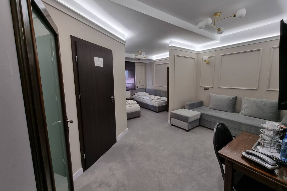 Une chambre d’hôtel avec un lit, un canapé, un bureau avec un téléphone et des lunettes, et une porte avec une pancarte.