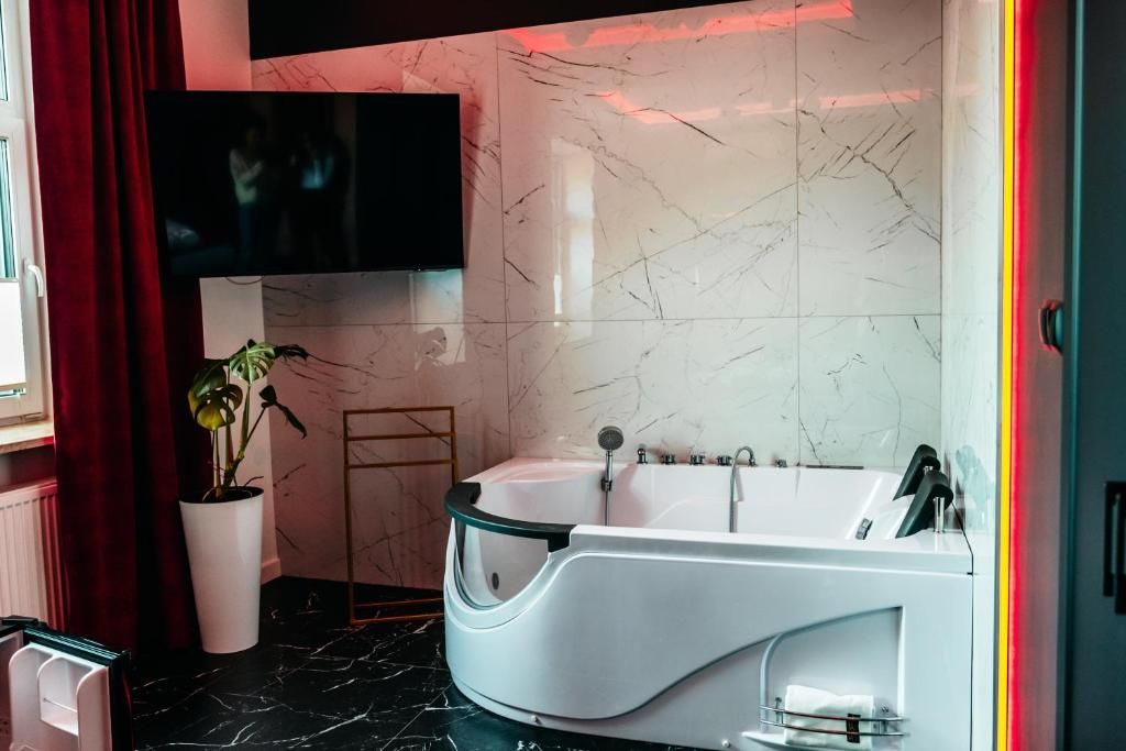 A modern bathroom with a freestanding bathtub, a potted plant, and a flat-screen TV mounted above the tub.