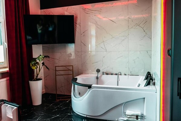 A modern bathroom with a freestanding bathtub, a potted plant, and a flat-screen TV mounted above the tub.