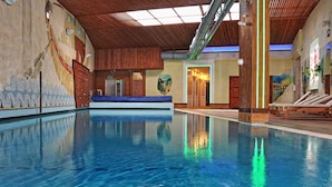 Een binnenzwembad met helder water, een houten plafond en een muurschildering.