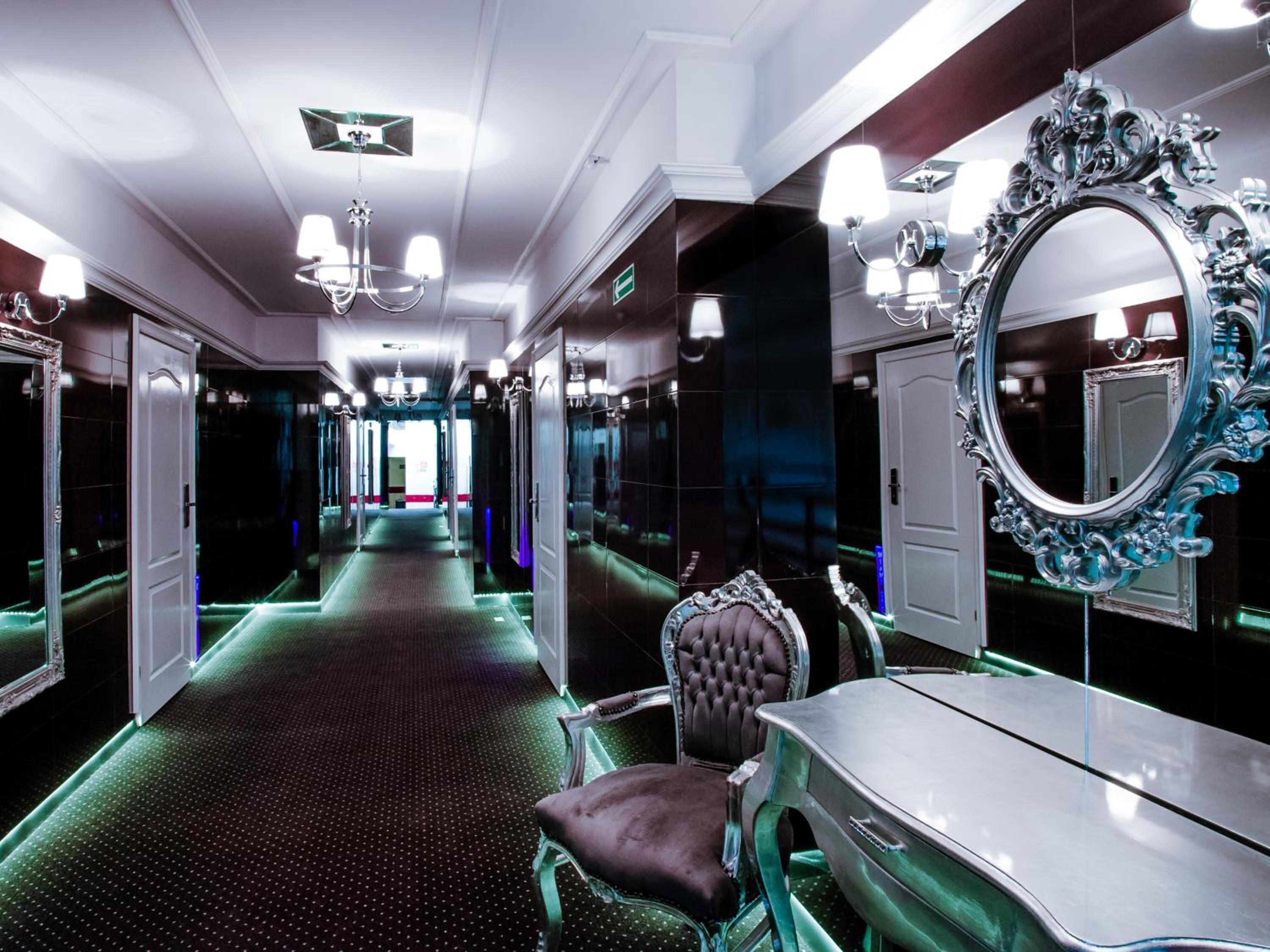A luxurious hallway with mirrored walls, a chandelier, and a classic vanity with a mirror.