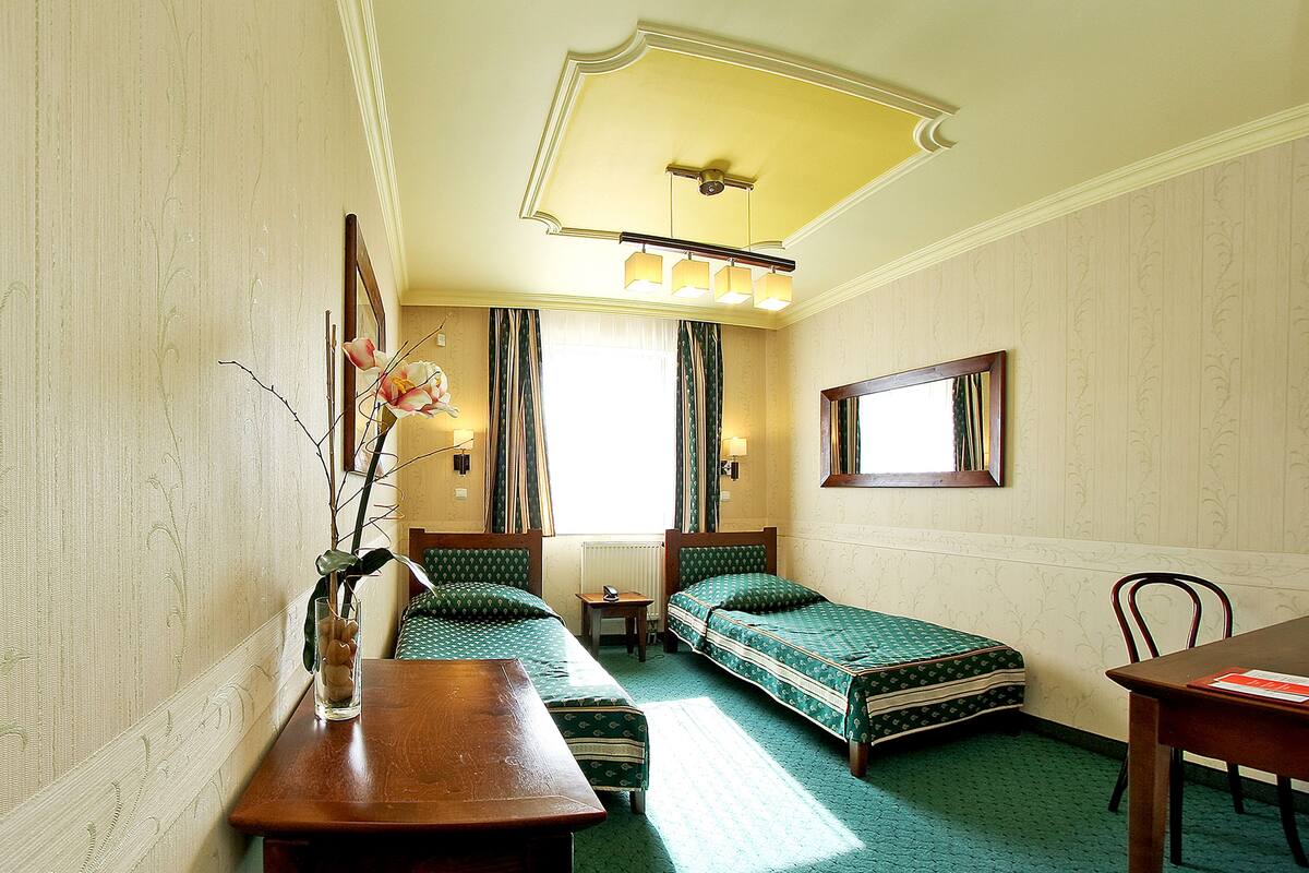 Une chambre d’hôtel avec deux lits simples, une table en bois, une chaise, une petite table avec une lampe et un miroir au mur.