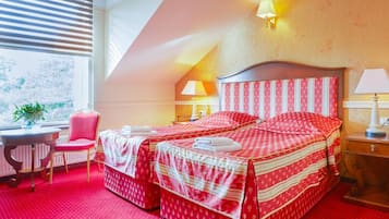 Habitación de hotel con una cama grande, dos lámparas de noche, una silla, una mesita y una ventana con persianas.