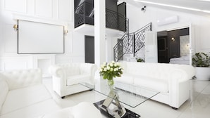 Een moderne woonkamer met witte meubels, een glazen salontafel en een trap met zwarte leuningen.