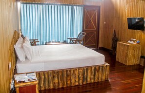 A hotel room with a wooden bed, a desk with a chair, a television, and a window with curtains.