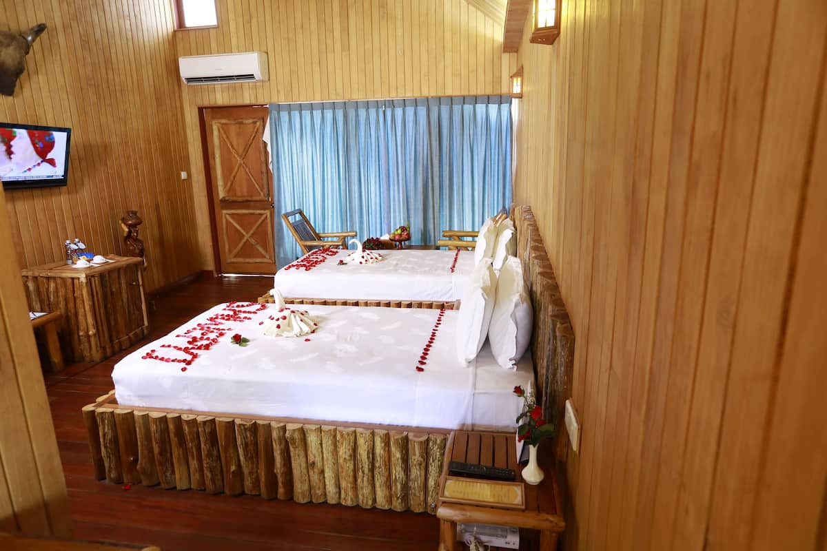 Una habitación con paneles de madera, una cama, dos sillas, una mesita y un televisor.
