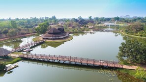 A traditional building with a thatched roof, a wooden bridge, and a pond with boats.
