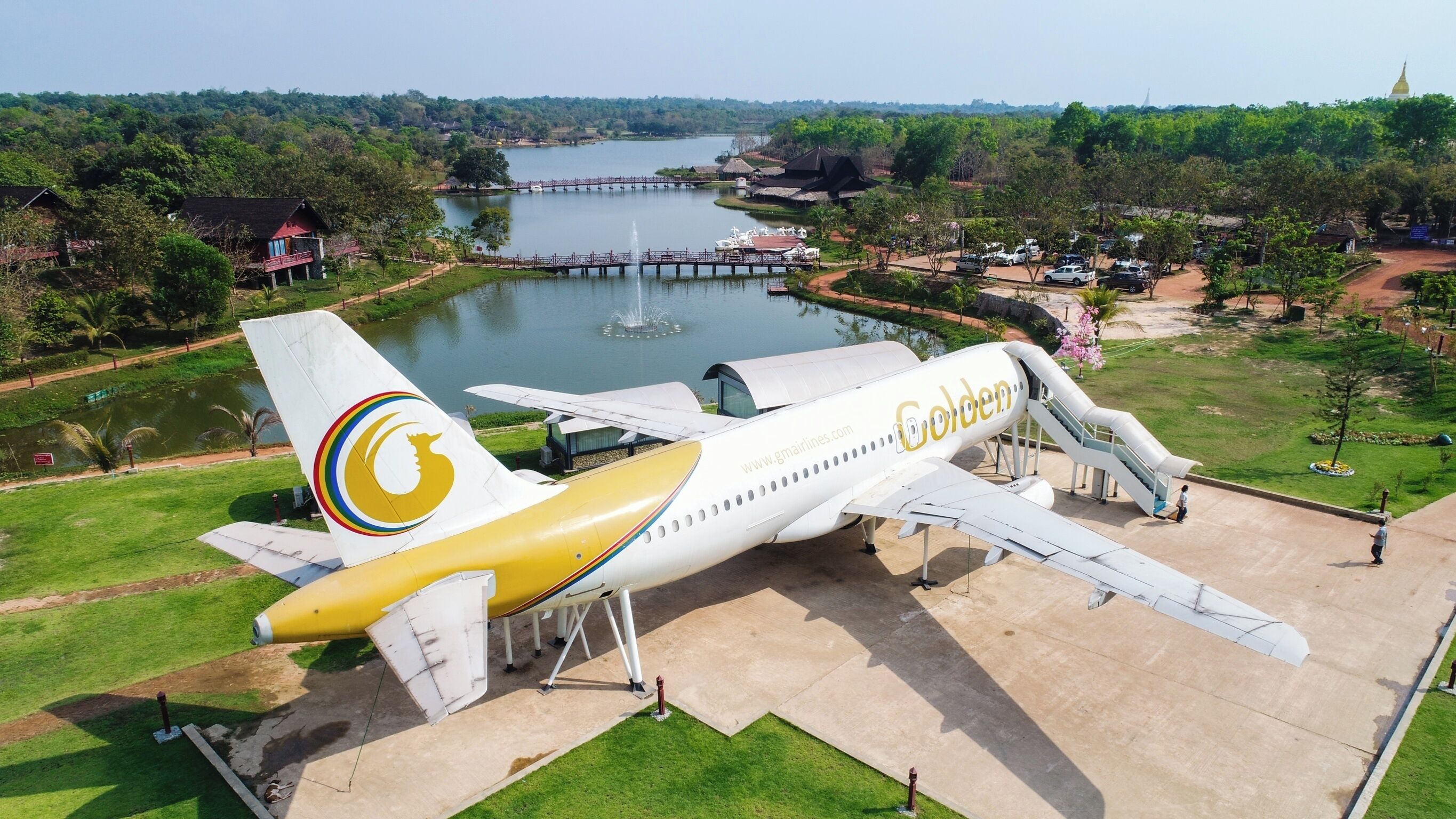 A Golden Airways airplane parked at an airport with a lake and greenery in the background.