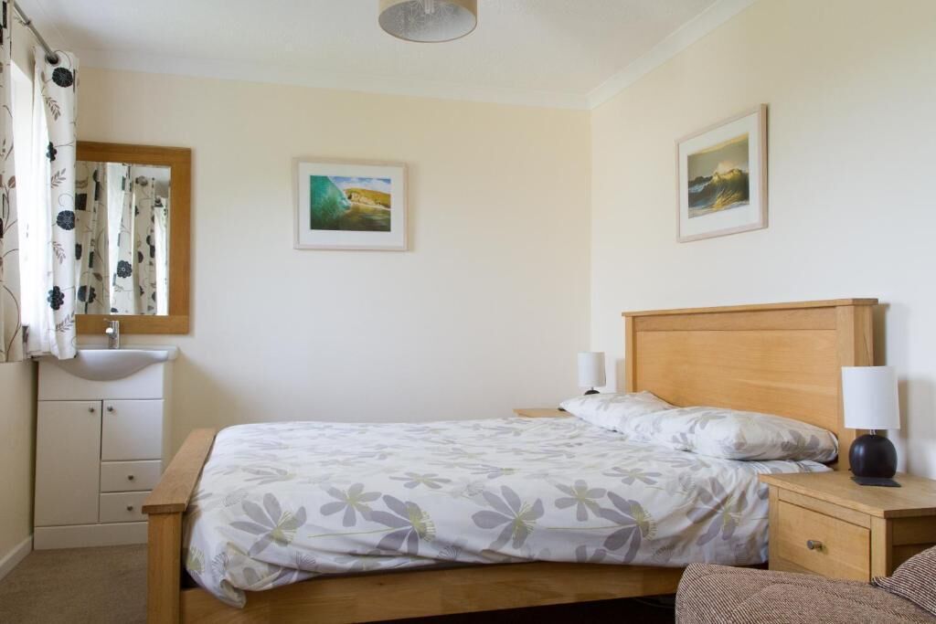 A bedroom with a bed, bedside tables, a nightstand, a mirror, and a wall-mounted sink.