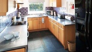 A modern kitchen with wooden cabinets, a black refrigerator, a microwave, and a toaster. - Gwithian Holidays, Godrevy House (Hayle)