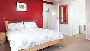 A bedroom with a bed, a nightstand, a dresser, and a door leading to another room. - Gwithian Holidays, Godrevy House (Hayle)