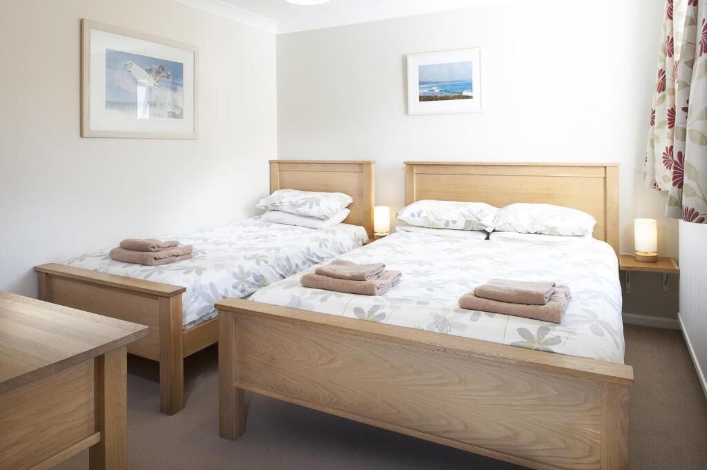 Une chambre d’hôtel avec deux lits en bois, du linge de lit blanc et une petite table de chevet avec une lampe.