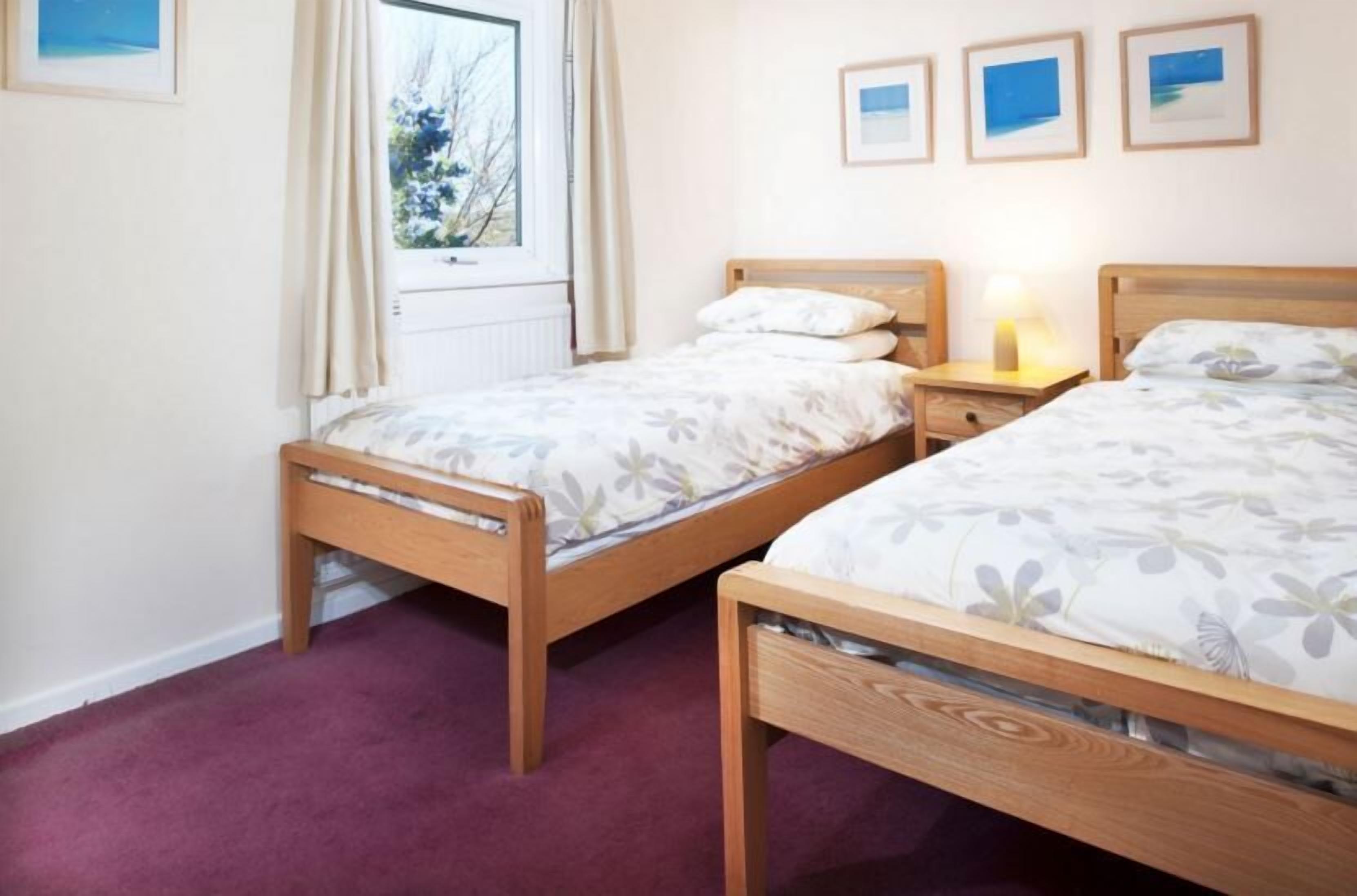 Un dormitorio con dos camas de madera, una ventana con cortinas y tres cuadros en la pared.