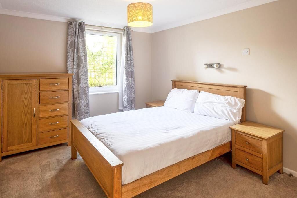 Un dormitorio con cama de madera, mesita de noche, armario y ventana con cortinas.