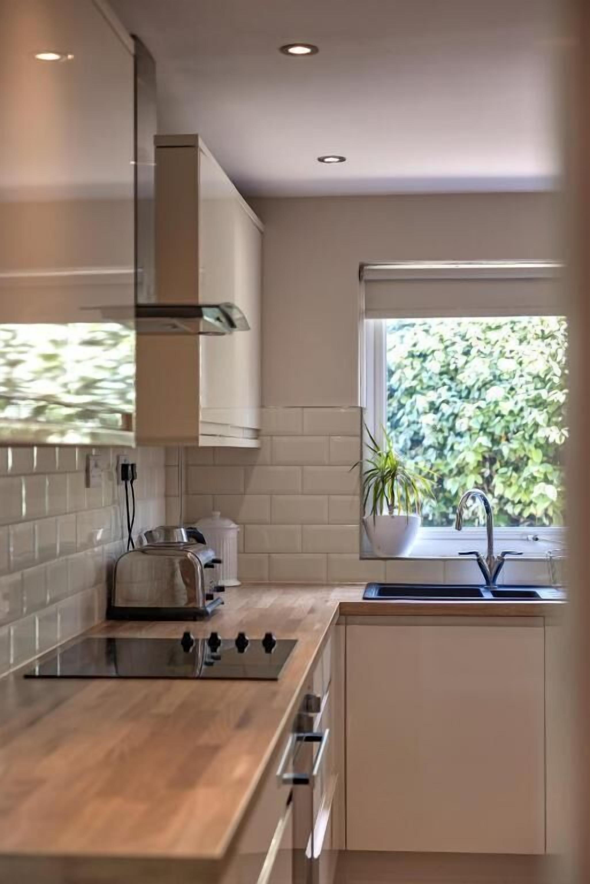 Una cocina moderna con estufa integrada, una ventana con vistas a la vegetación y un salpicadero de azulejos blancos.