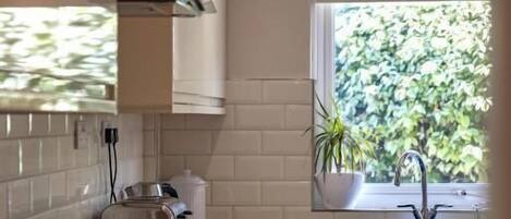 Una cocina moderna con estufa integrada, una ventana con vistas a la vegetación y un salpicadero de azulejos blancos.