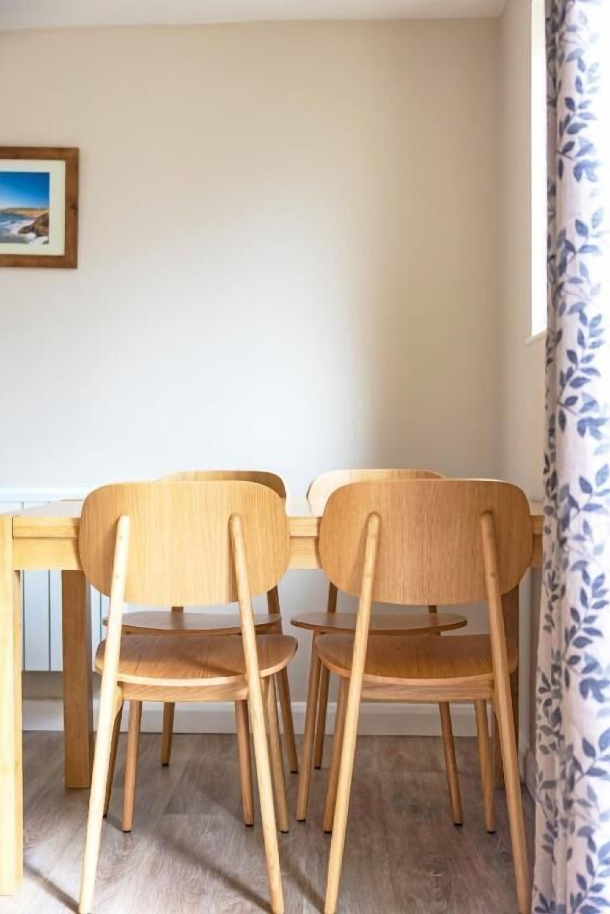 A dining area with a wooden table and chairs, a framed picture on the wall, and a window with a curtain.