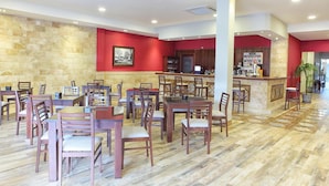 A spacious restaurant with multiple tables and chairs, a counter with a menu, and a stone wall. - Hostal Garlu (La Rambla)