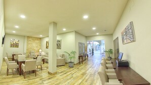 A spacious hotel lobby with a long reception desk, multiple seating areas, and a decorative plant. - Hostal Garlu (La Rambla)
